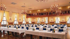 Un espai per a banquet amb diverses taules preparades per a esdeveniments, lluminàries i grans finestres amb cortines.