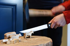 Eine Person hält ein Messer und arbeitet an einem hölzernen Pferdemodell auf einem Baumstumpf.