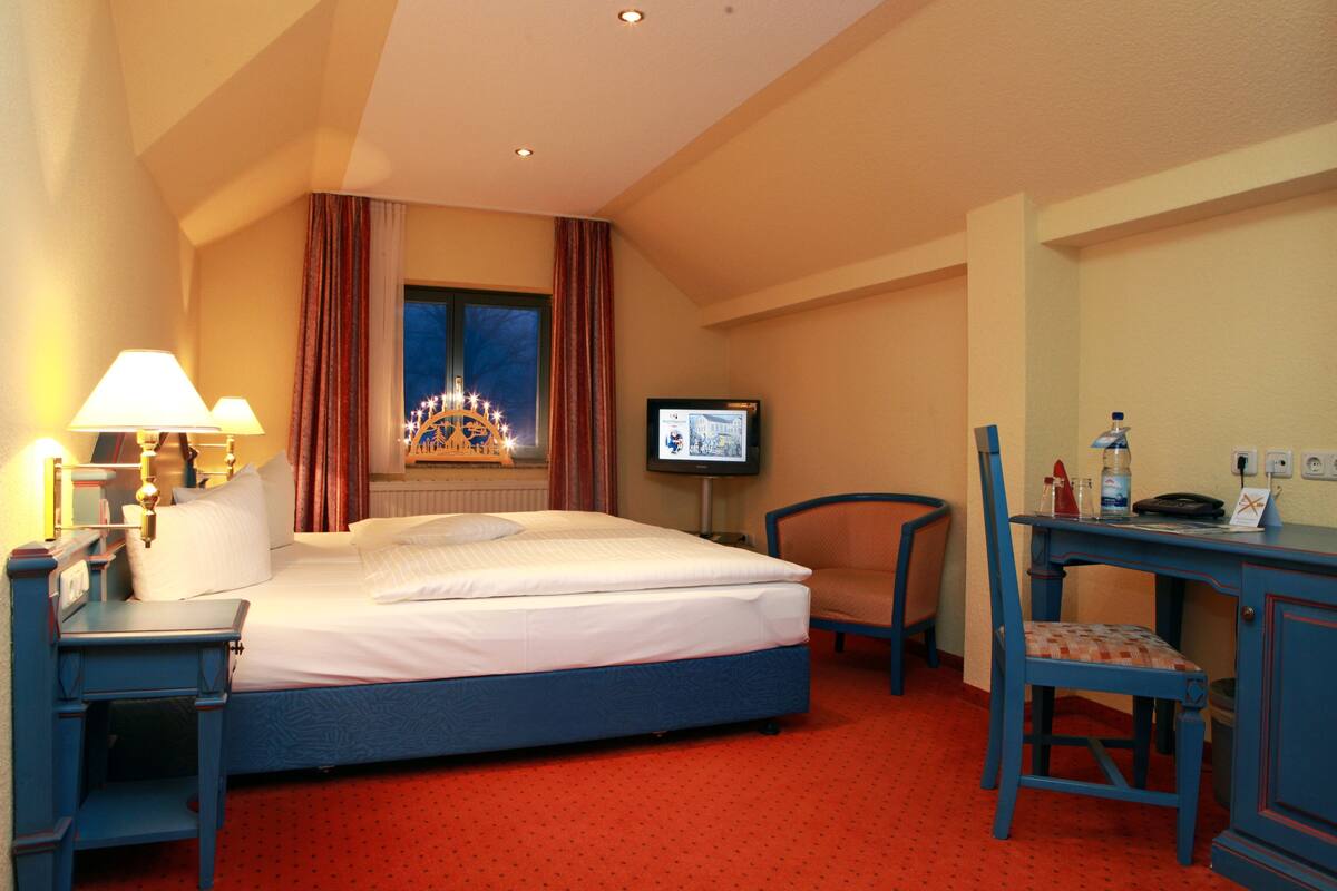 Une chambre d’hôtel équipée d’un lit, d’un bureau, d’une chaise, d’une télévision et d’une fenêtre avec des rideaux.