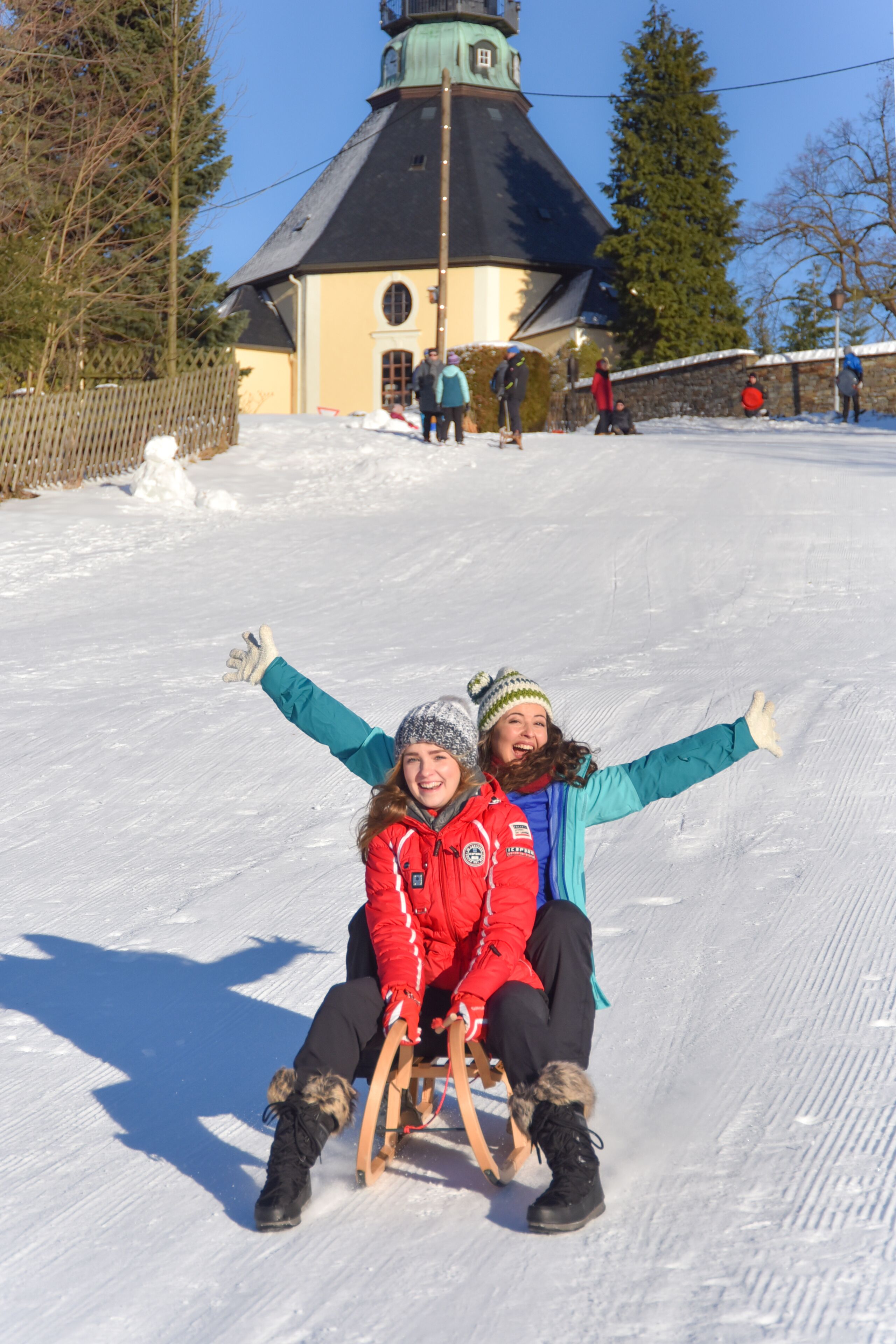 A snowy outdoor area with a wooden sled and two people sitting on it.