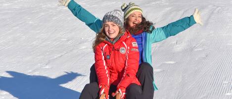 A snowy outdoor area with a wooden sled and two people sitting on it.