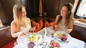 Dues persones dinant a una taula amb plats de menjar, gots de vi i una espelma.