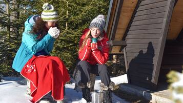 Two people sitting on a wooden bench outdoors with a metal container in front of them.