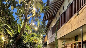 A narrow pathway flanked by lush greenery and a building with a balcony. - Villa Puriartha (Ubud)