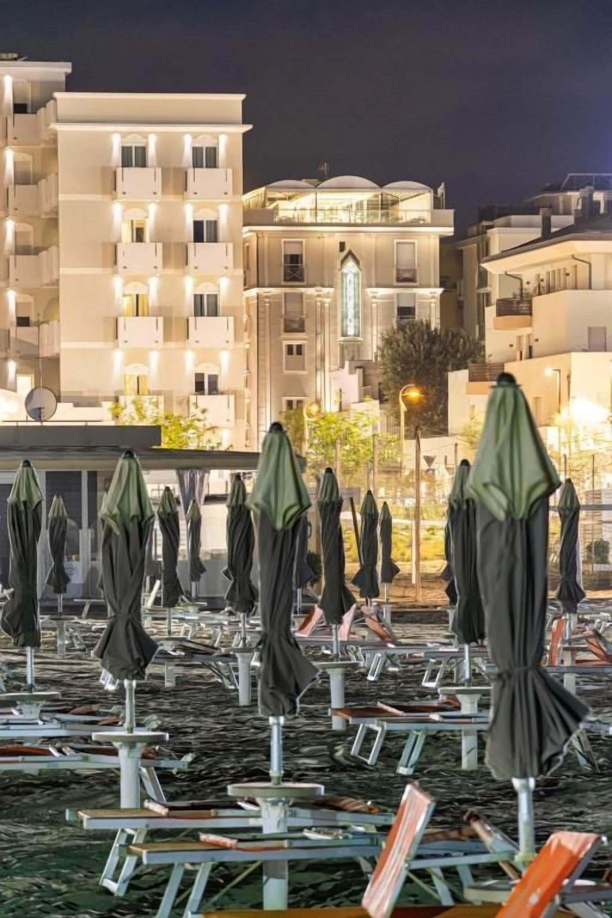 File di ombrelloni da spiaggia e lettini su una terrazza panoramica, con edifici sullo sfondo.