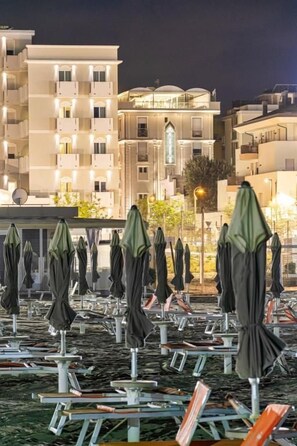A row of beach umbrellas and lounge chairs on a rooftop terrace with buildings in the background. - Hotel Augustus (Rimini)