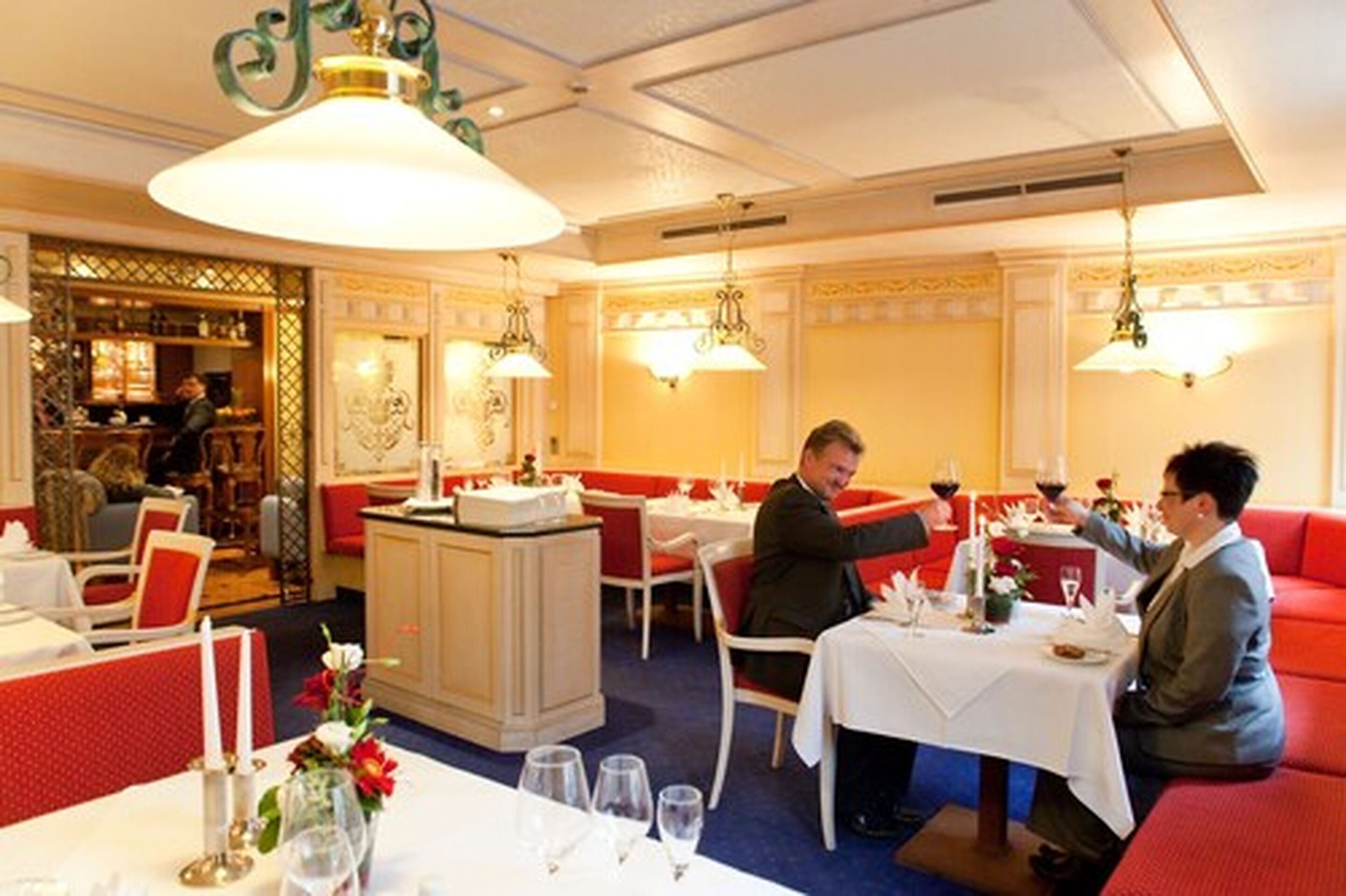 A restaurant with red upholstered booths, white tables, and chandeliers.