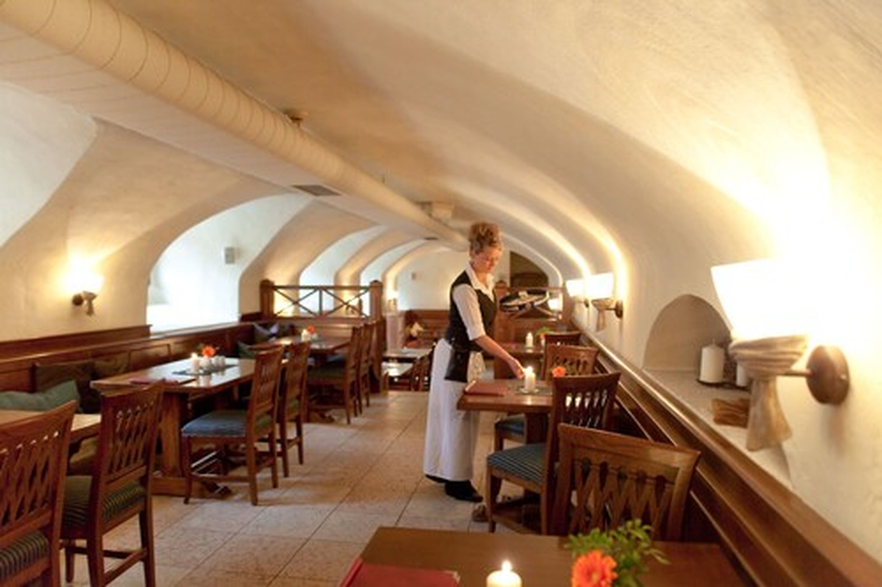 A restaurant with wooden furniture, a waitress, and a vaulted ceiling.