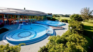 Un amplio espacio exterior con piscina que incluye varias piscinas y un edificio con fachada de vidrio.