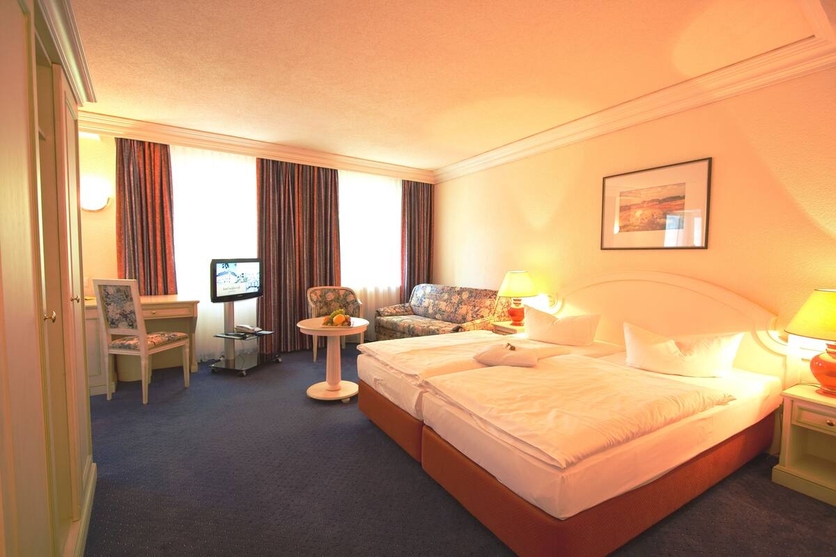 A hotel room with a bed, two bedside tables, a desk, a chair, a small table with fruit, and a television.