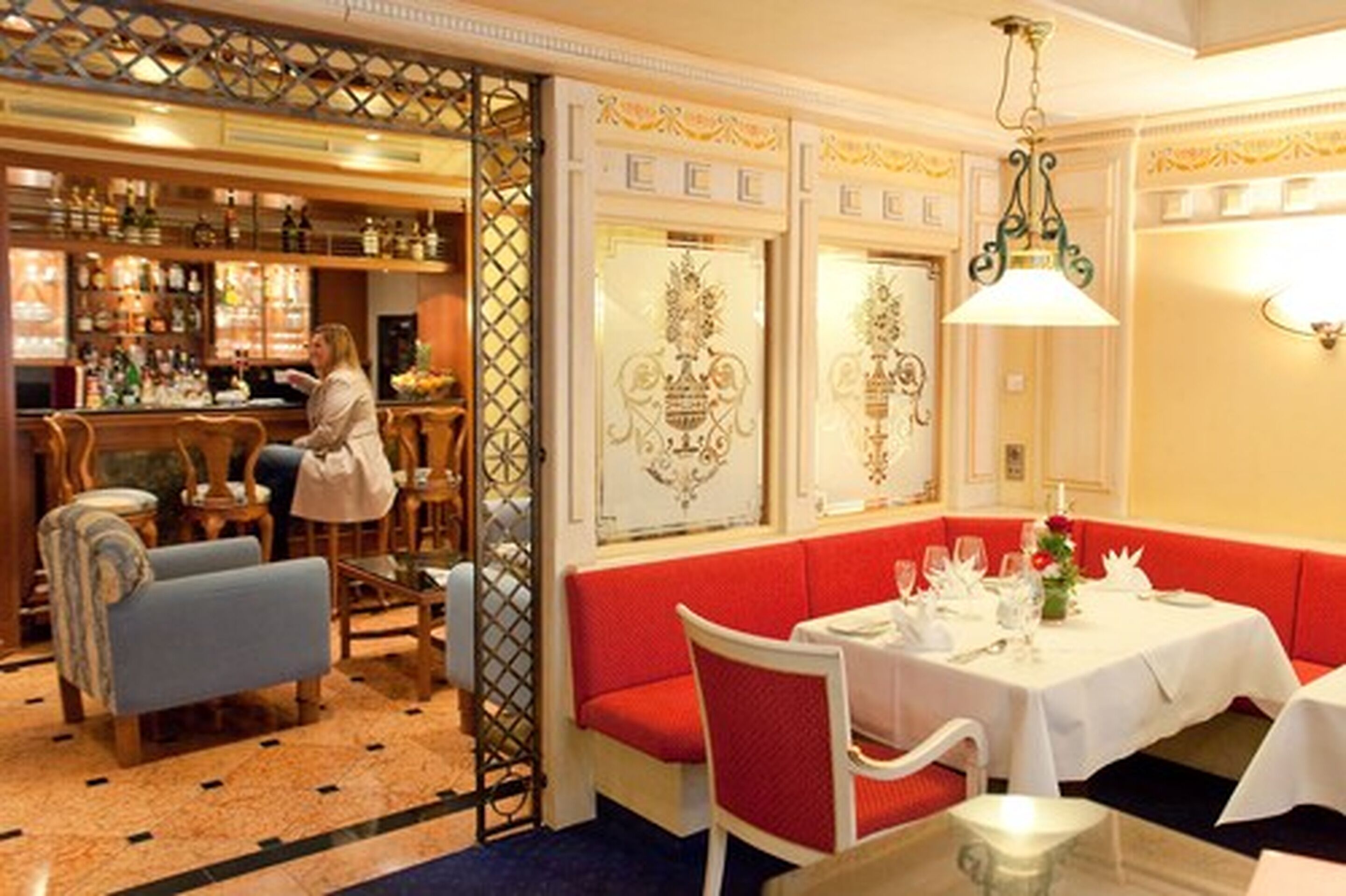 A bar area with a bartender, a seating area with red cushioned benches, and a table set for dining.