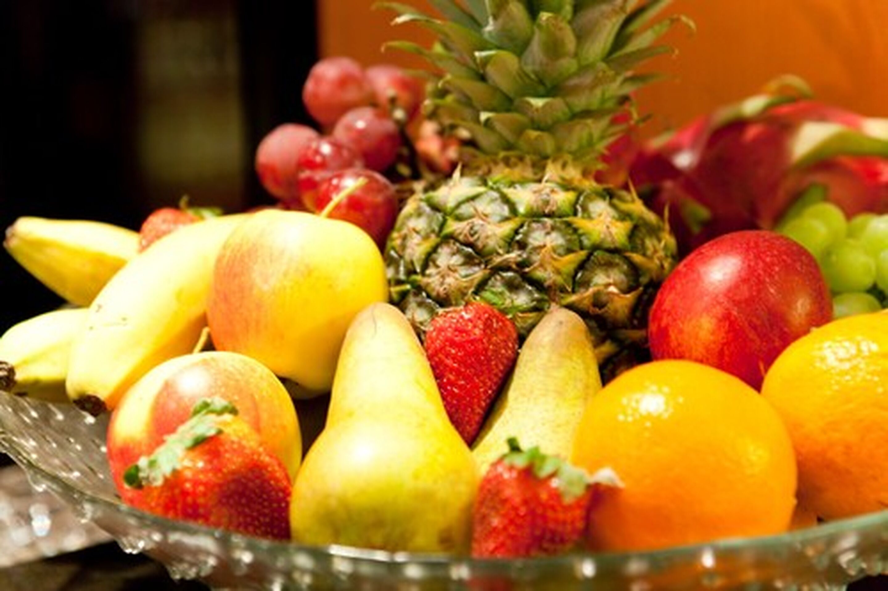 Eine Glasschüssel mit verschiedenen Früchten, darunter Bananen, Äpfel, Birnen, Erdbeeren und Trauben.
