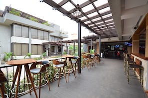 An outdoor cafe area with tables and chairs, a pergola, and a view of a building with balconies. - The Venti Hotel & Spa (Kampala)