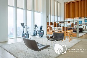 Relax in a spacious living area with a city view, featuring a seating area, bookshelf, and exercise bikes.
