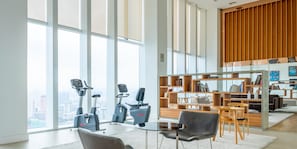 A modern living room with a large window, two exercise bikes, a coffee table, and a bookshelf.
