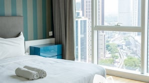 A hotel room with a large bed, a view of the city through a window, and a blue bedside table.