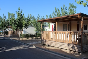 A row of mobile homes with wooden decks and railings, a clear sky, and a street in the foreground. - Camping Fayón Fishing (Fayon)