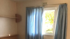 Una cama individual con una colcha estampada, dos toallas enrolladas y una ventana con cortinas azules.