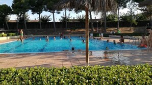 Una piscina con múltiples carriles, rodeada por una solana con baldosas y una sombrilla de paja.