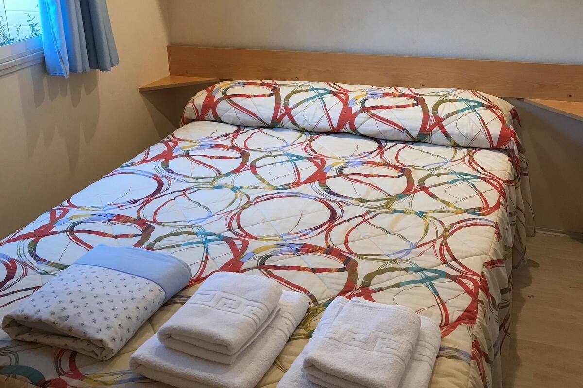 A neatly made bed with a colorful patterned bedspread and three folded towels.