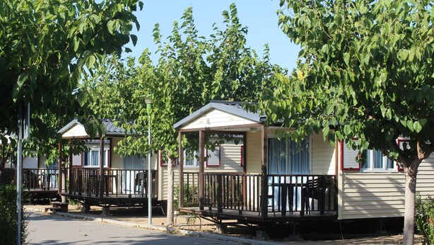 Una hilera de casas móviles con porches y barandillas, ubicadas en una zona residencial con árboles.