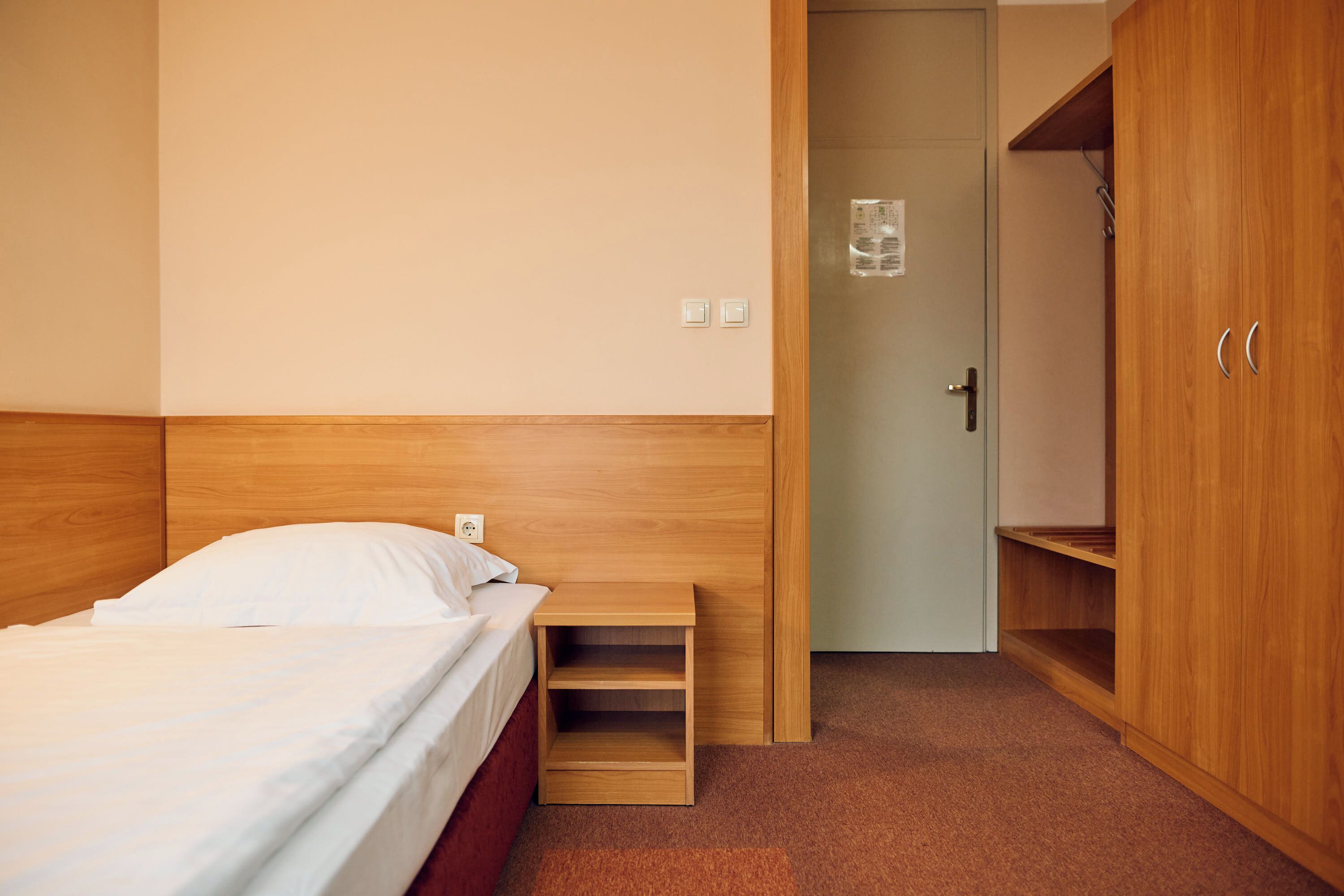 Un dormitorio con una cama, una mesita de noche de madera, un armario y una puerta con manija.