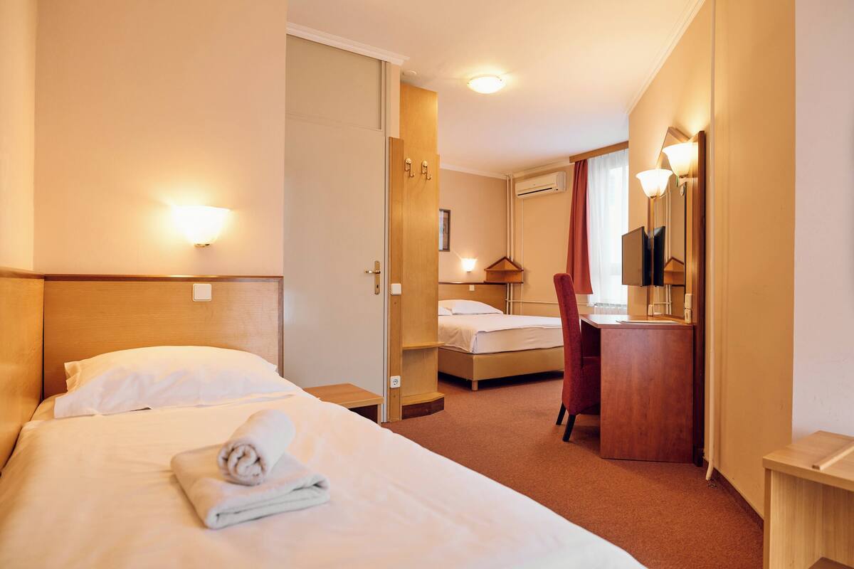 A hotel room with a bed, a desk, a chair, a mirror, and a wardrobe.