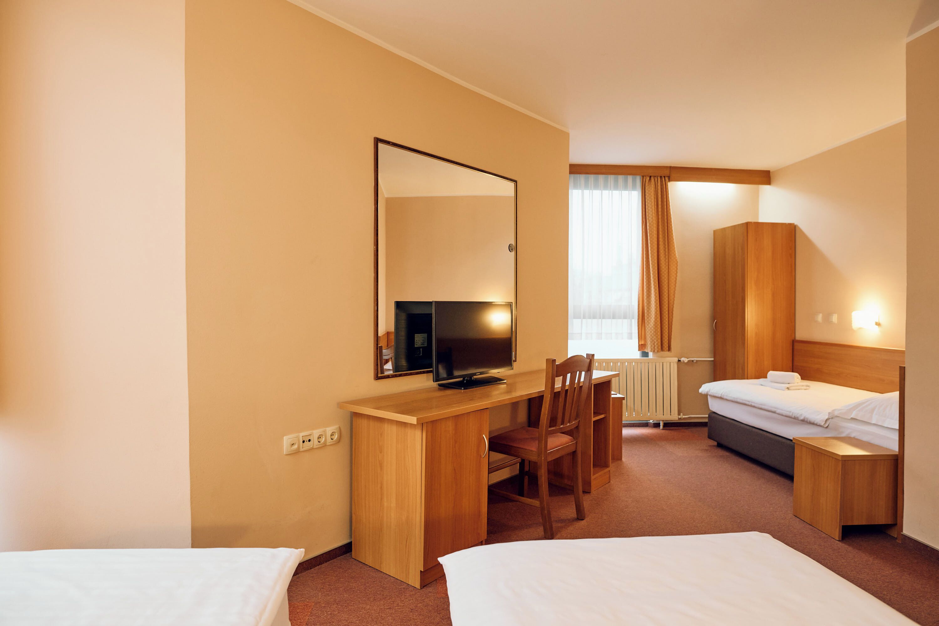 A hotel room with a bed, a desk with a chair, a television, and a wardrobe.