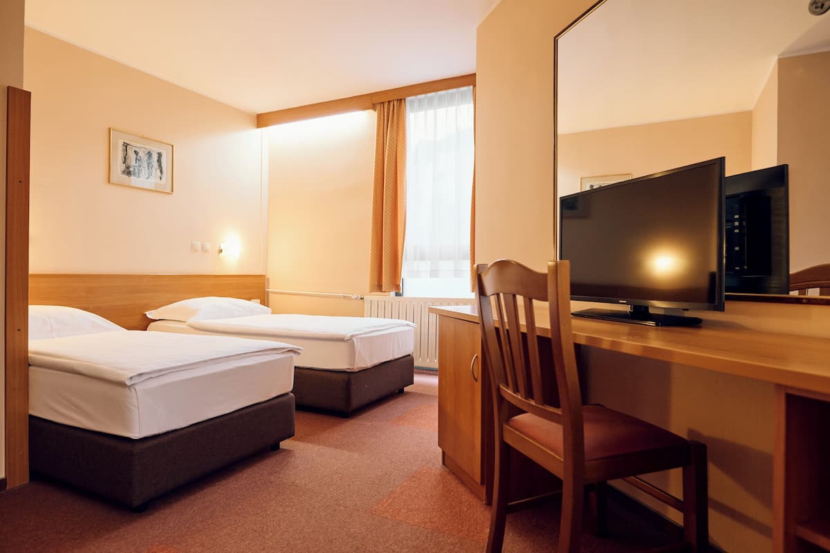 A hotel room with two beds, a desk with a television, and a chair.