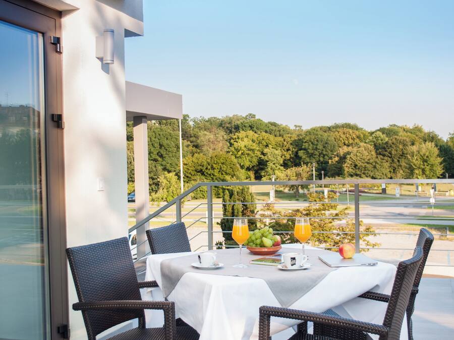 A balcony with a table set for breakfast, wicker chairs, and a view of a park and river.