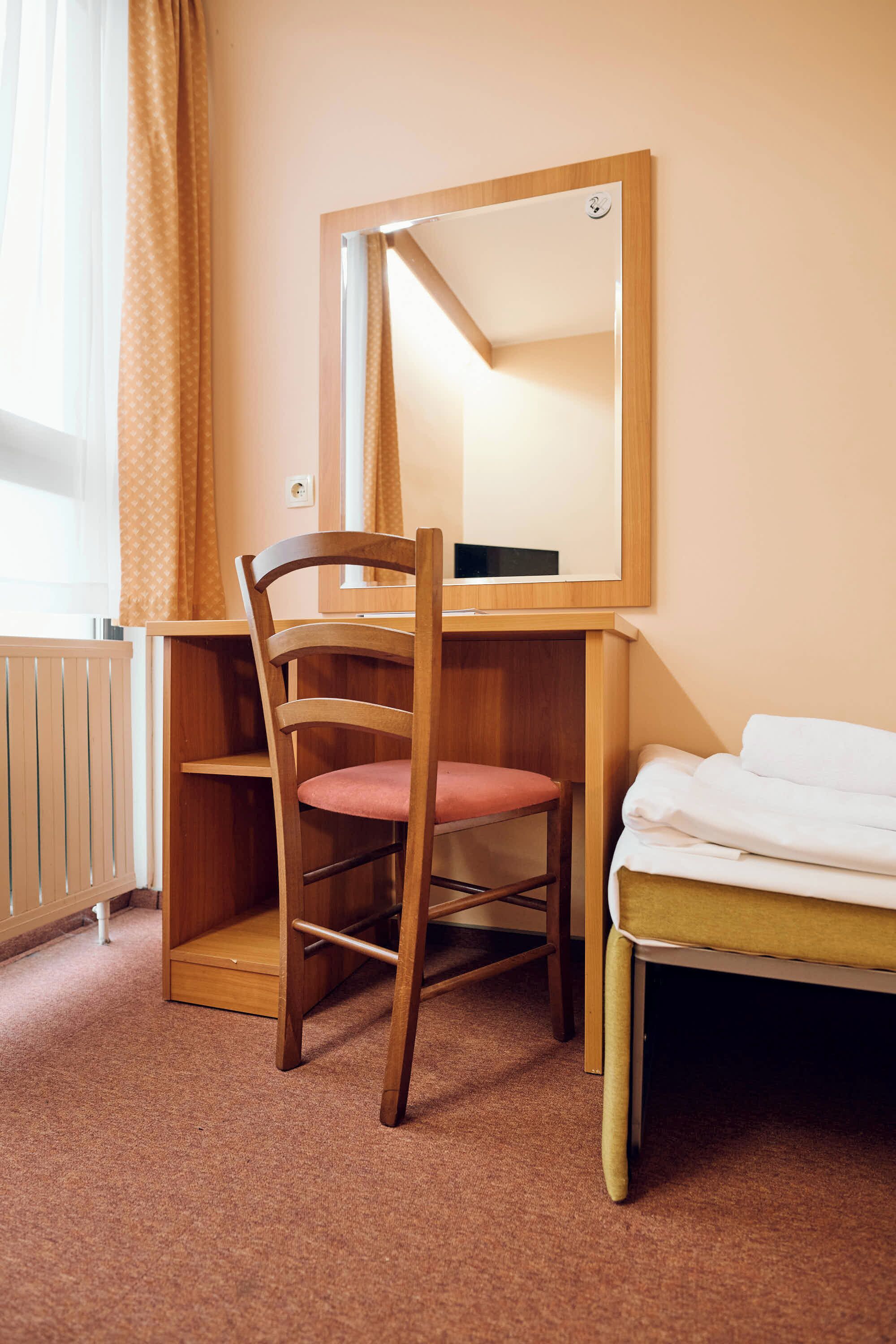 A hotel room with a wooden desk, a chair, a bed, and a large mirror.