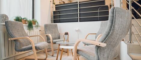 A modern living room with three grey upholstered chairs, a round wooden table, and a view of a staircase.