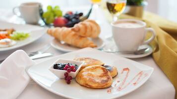 Colazione con croissant, pancake e una ciotola di frutti di bosco su un piatto bianco.