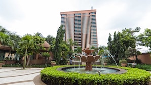 A courtyard with a central fountain, surrounded by well-maintained hedges and palm trees, with a tall building in the background. - Times Square 1 by Plush (Kuala Lumpur)