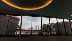 A modern interior with large windows offering views of the Petronas Towers and a traditional building. - Times Square 1 by Plush (Kuala Lumpur)