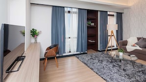 A modern living room with a flat-screen TV, a wooden desk, a comfortable sofa, a coffee table, and a large window with curtains. - Times Square 1 by Plush (Kuala Lumpur)