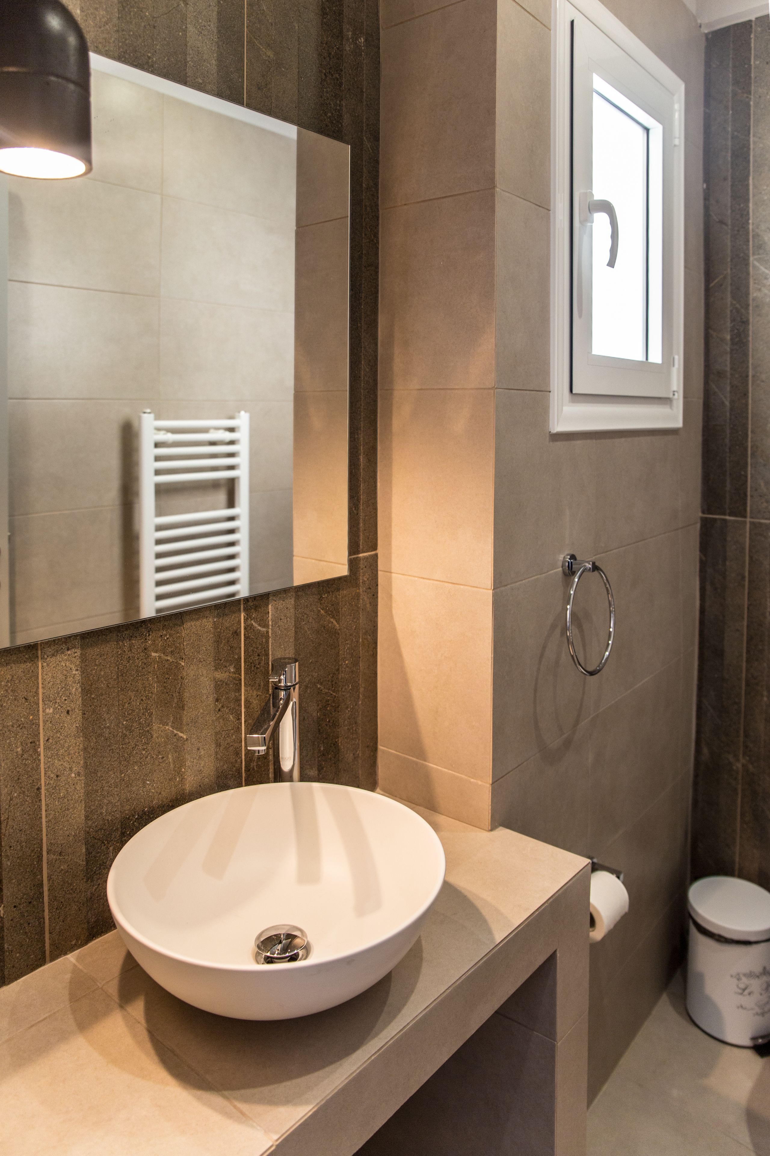 A modern bathroom with a round sink, a mirror, a towel rack, and a toilet.