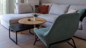 Un salon moderne avec un canapé, une table basse ronde et un fauteuil vert. Trois œuvres d’art sont accrochées au mur et représentent des figures abstraites.