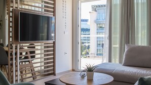 Un salon moderne avec un canapé, un fauteuil vert, une table ronde en bois et un téléviseur posé sur un meuble en bois.