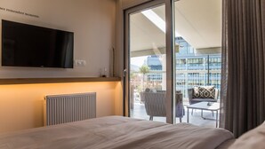 Une chambre d’hôtel avec un grand lit, un téléviseur à écran plat fixé au mur et un balcon offrant une vue sur la ville.