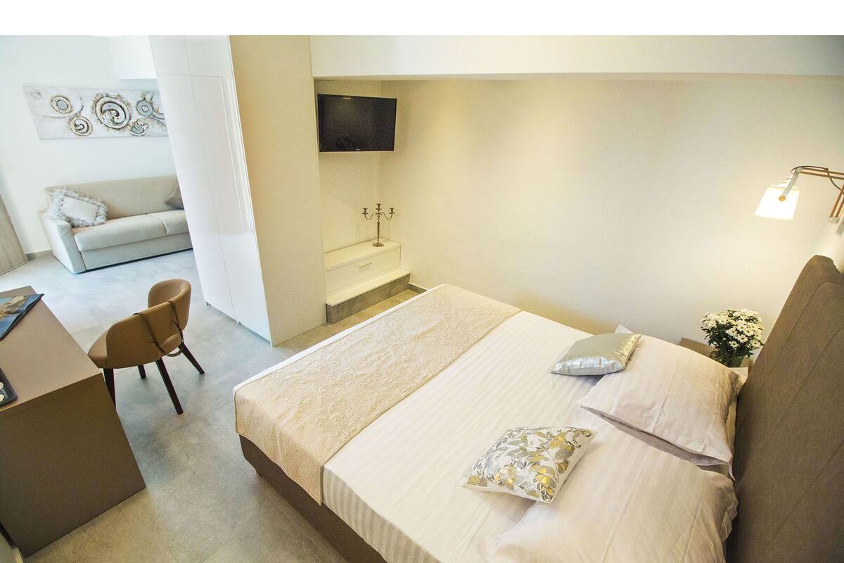A modern bedroom with a large bed, a desk, and a TV mounted on the wall.