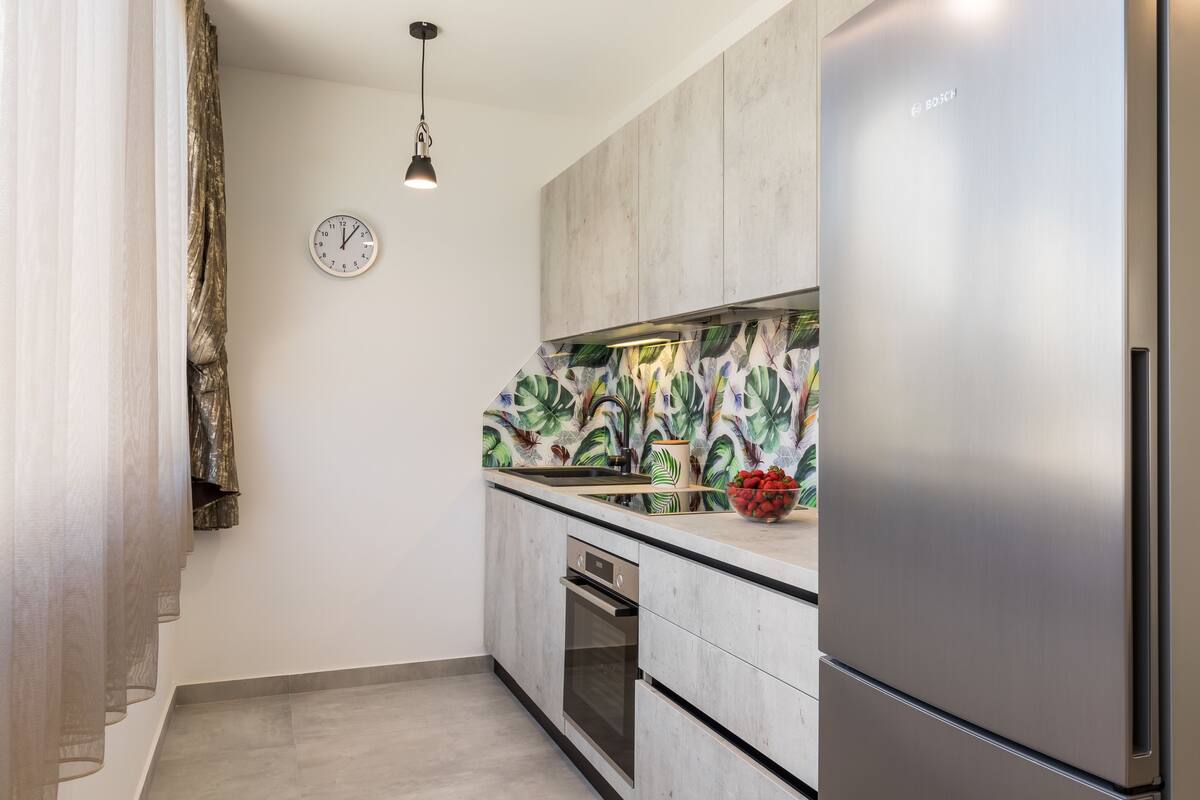 A modern kitchen with a stainless steel refrigerator, a built-in oven, and a clock on the wall.