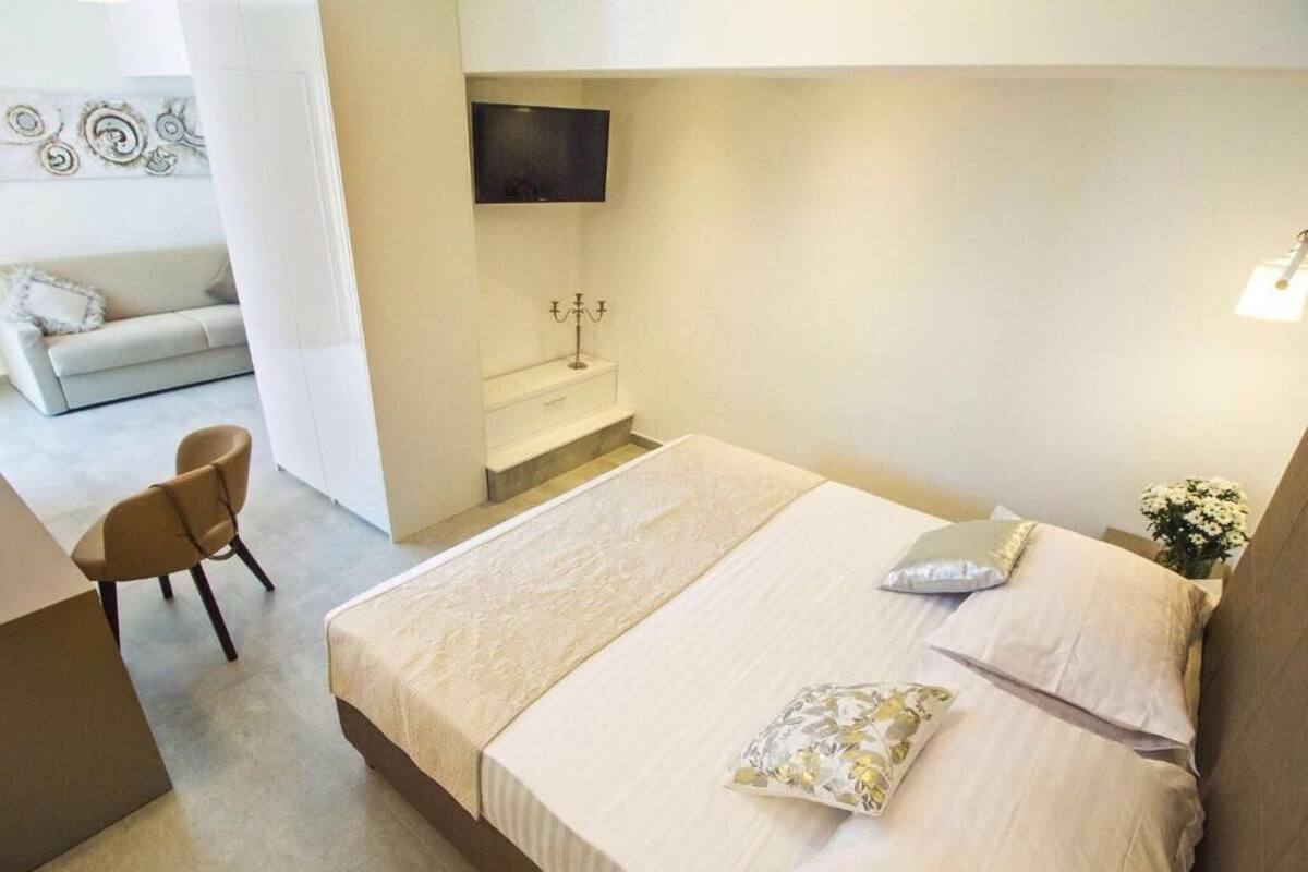 A hotel room with a bed, a desk, a chair, a TV mounted on the wall, and a small bathroom area.