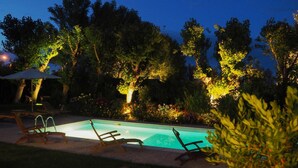 A swimming pool with lounge chairs and an umbrella, surrounded by trees and illuminated by artificial lighting. - Villa Mirella Beach (Fermo)