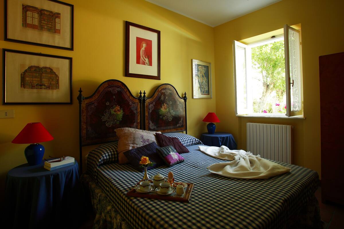 A neatly arranged bedroom with a checkered bedspread, a bedside table with a lamp, and framed artwork on the wall.
