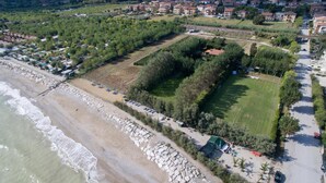An aerial view of a coastal area with a beach, a park with trees, and residential buildings in the background. - Villa Mirella Beach (Fermo)