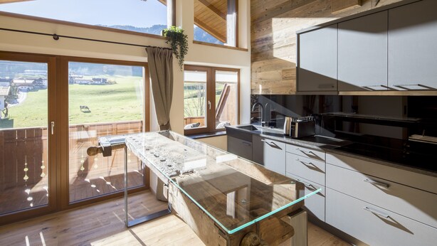 Una cocina moderna con una isla de vidrio, armarios de madera y ventanas amplias que ofrecen vistas a un paisaje verde.