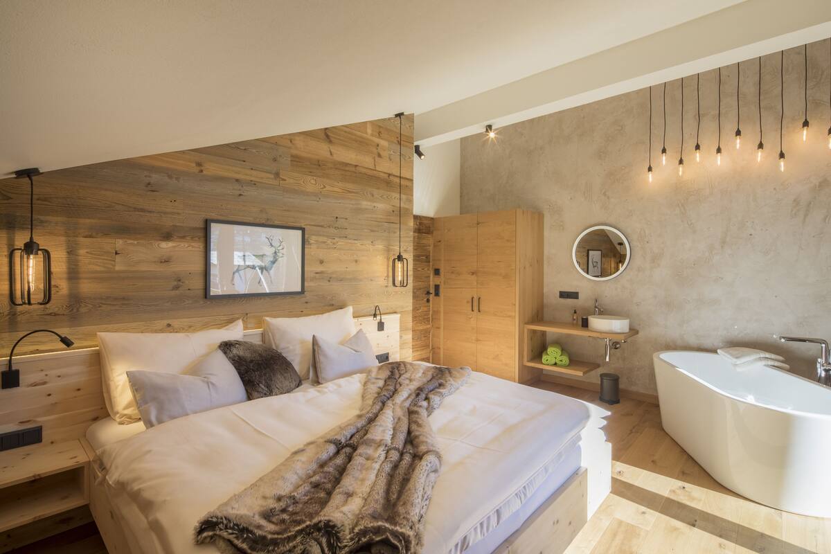 Un dormitorio moderno con cabecera de madera, una cama grande con ropa blanca, una manta suave y un armario empotrado. En la mesita de noche, una lámpara.