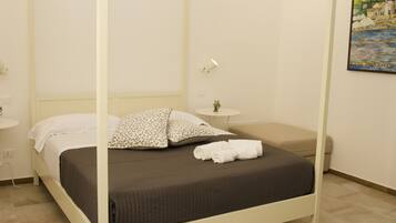 A four-poster bed with a dark brown bedspread and white pillows, a small bedside table with a lamp, and a painting on the wall.