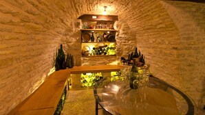 Una bodega rústica de piedra con estantes llenos de botellas de vino y una vitrina central con copas de vino.